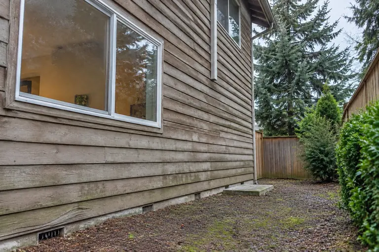 Ductless heat pump installed on a two-story home, before: Before installation, the side yard shows the existing concrete pad awaiting the new air conditioning unit.