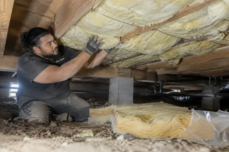 A technician installs new under-floor insulation in a crawl space.