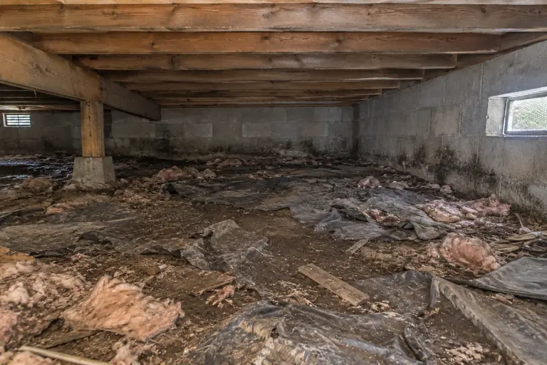 Crawl space cleaning with debris and vapor barrier removal in Bellevue, before: The crawl space is heavily cluttered with torn vapor barrier and insulation debris, visibly dirty and in need of a thorough cleaning.