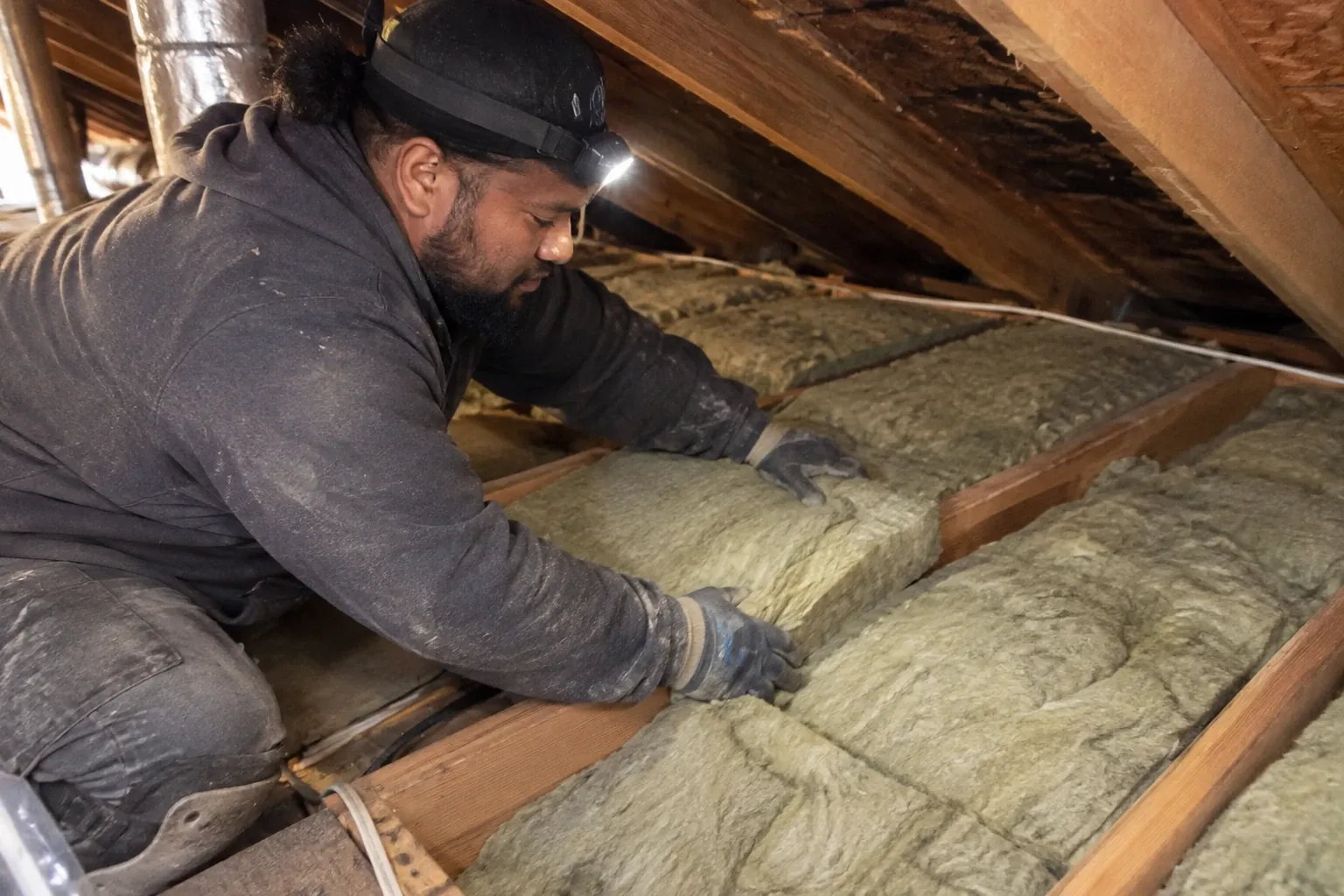 A technician installs fiberglass batts between attic joists.