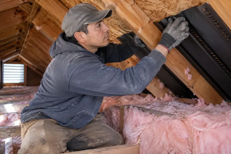 A technician is carefully installing attic soffit baffles to improve ventilation and insulation effectiveness in a residential attic space.