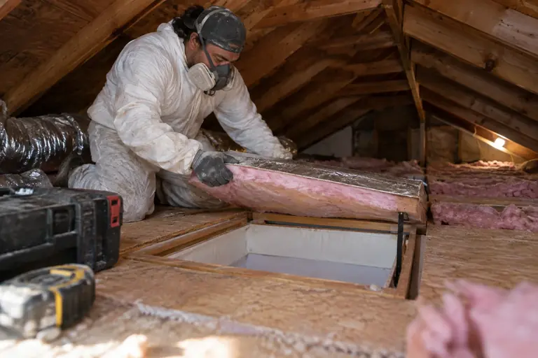 A technician is installing new insulation around an attic hatch.
