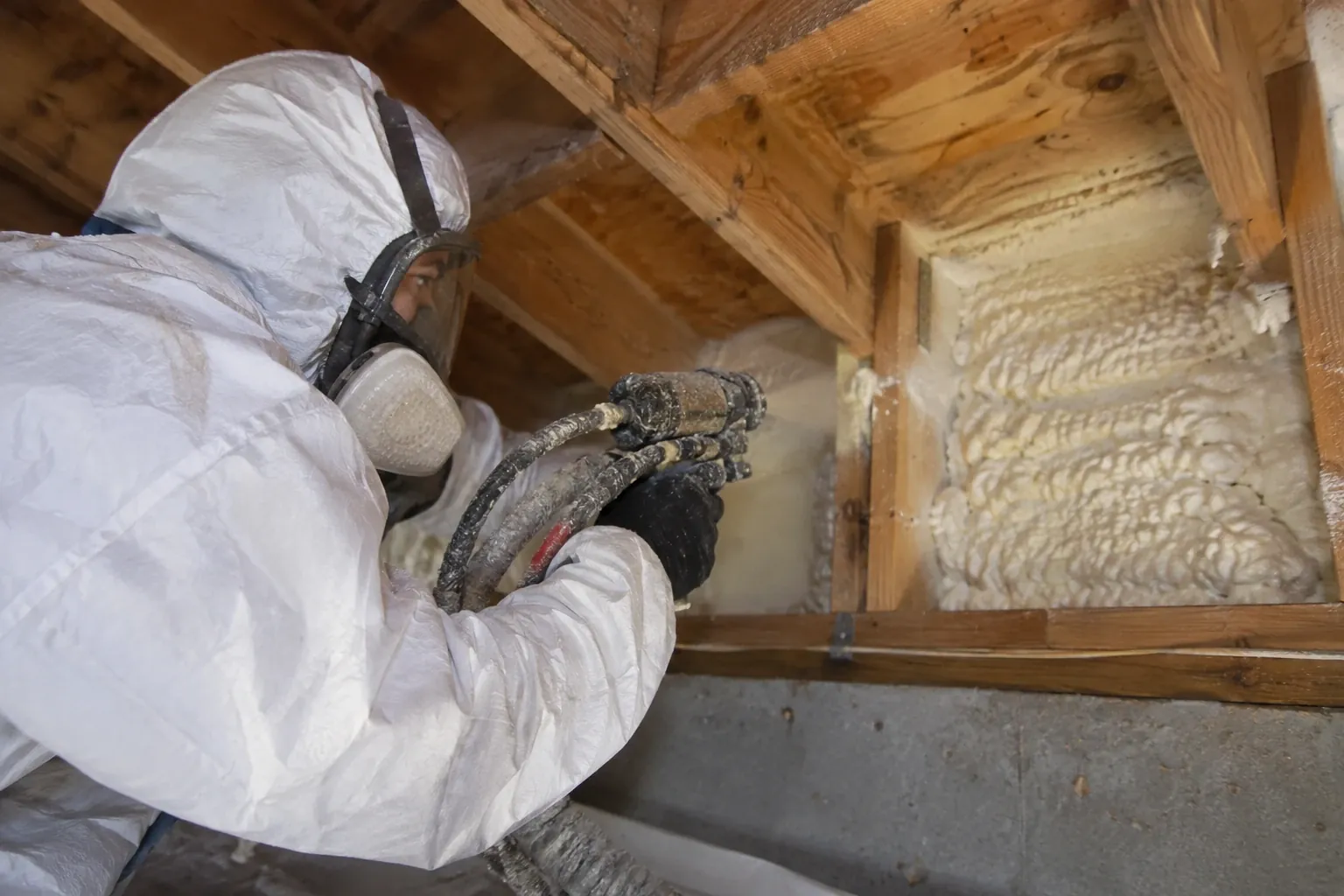 A technician sprays foam insulation into a wall cavity.