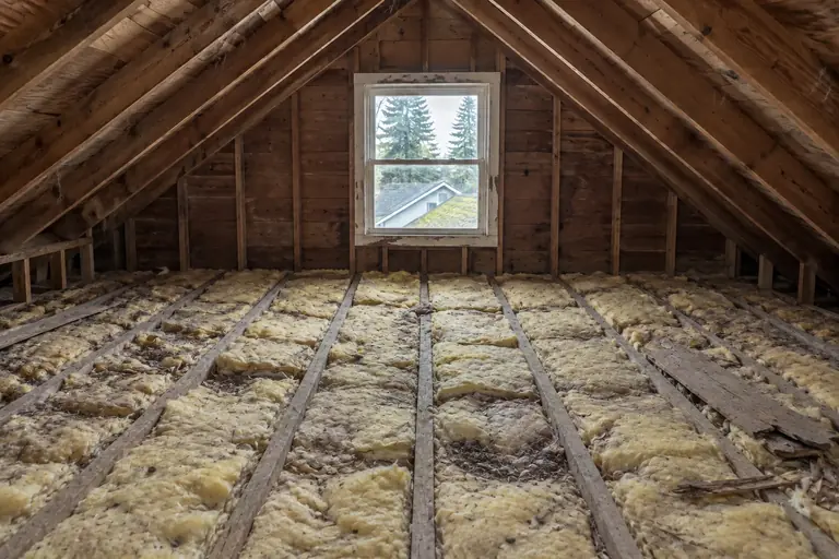 Attic insulation replacement in a Seattle Craftsman bungalow attic, before: The attic floor is covered with degraded yellow fiberglass batts and debris, offering poor thermal performance.