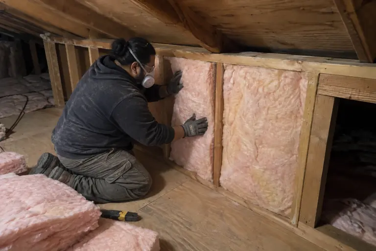 Insulating an uninsulated knee wall, in progress: A technician carefully fits new EcoBatt fiberglass insulation batts into the previously empty knee wall cavities.
