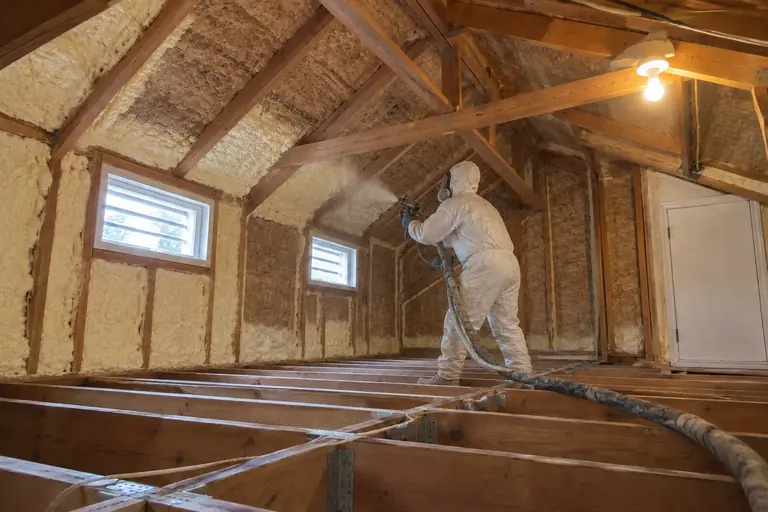 Spray foam attic insulation replacement in 1990s split-level home attic, in progress: Applying closed-cell spray foam insulation to the underside of the roof deck and rim joists, enhancing energy efficiency.