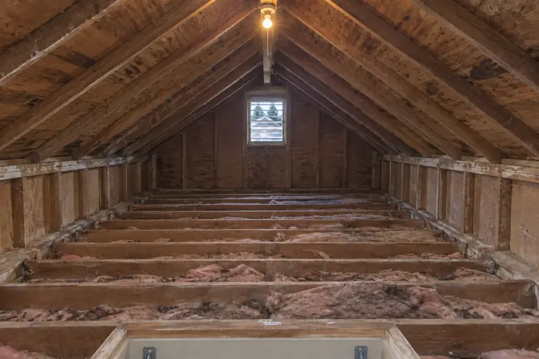 Spray foam insulation on an attic roof deck, before: The attic space shows aging and patchy insulation with bare roof decking and open knee walls, ready for professional insulation replacement.