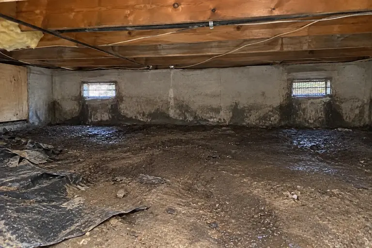 Moisture barriers in a vented crawl space on a mid-century rambler, before: The crawl space floor is bare and damp, with torn plastic debris and moisture clearly visible under the vents.