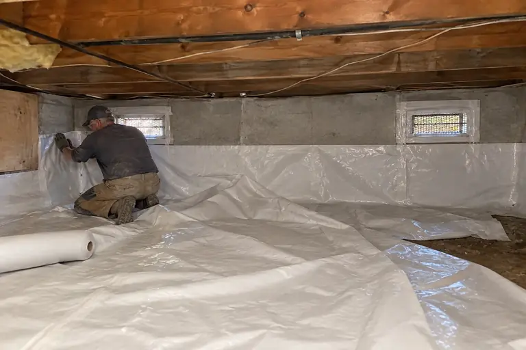 Moisture barriers in a vented crawl space on a mid-century rambler, in progress: A technician installs the new vapor barrier sheet, carefully positioning and.