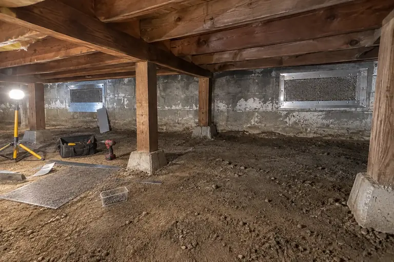 Crawl space rodent proofing in an Everett split-level, in progress: A technician is installing heavy-gauge steel mesh and sheet metal to fully seal the crawl space vents, preventing rodent access.