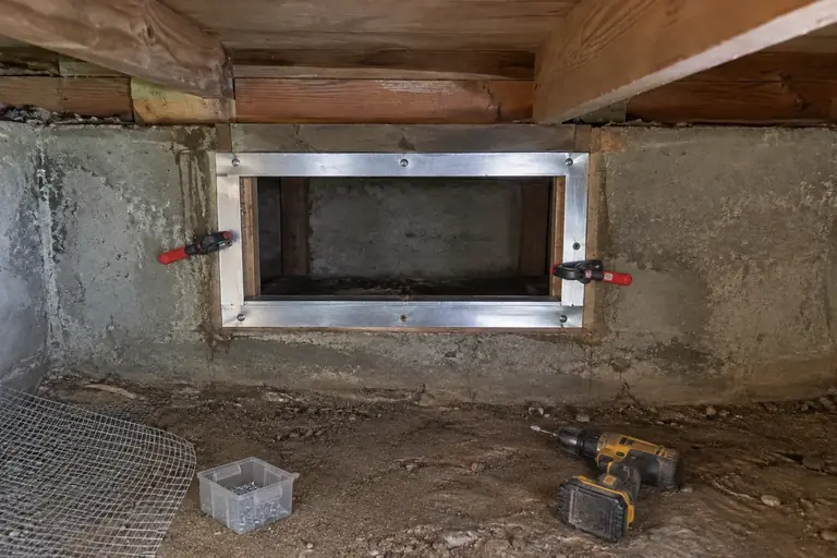 Crawl space vent sealing in Bellevue, in progress: The technician prepares the vent opening by fitting a new sheet metal frame to ensure a secure base for rodent exclusion.
