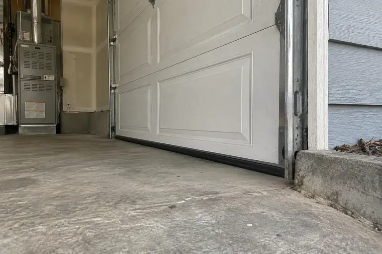 Garage door corner seal replacement, after: The new rubber door bottom seal is fully installed, closing the previous gap to prevent rodent entry.